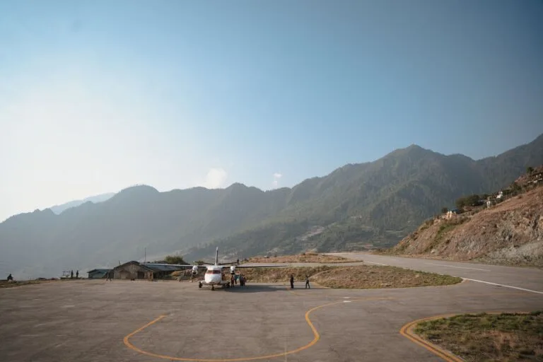 A scenic view of a small aircraft on a lukla airport surrounded by lush green hills under a vibrant blue sky.