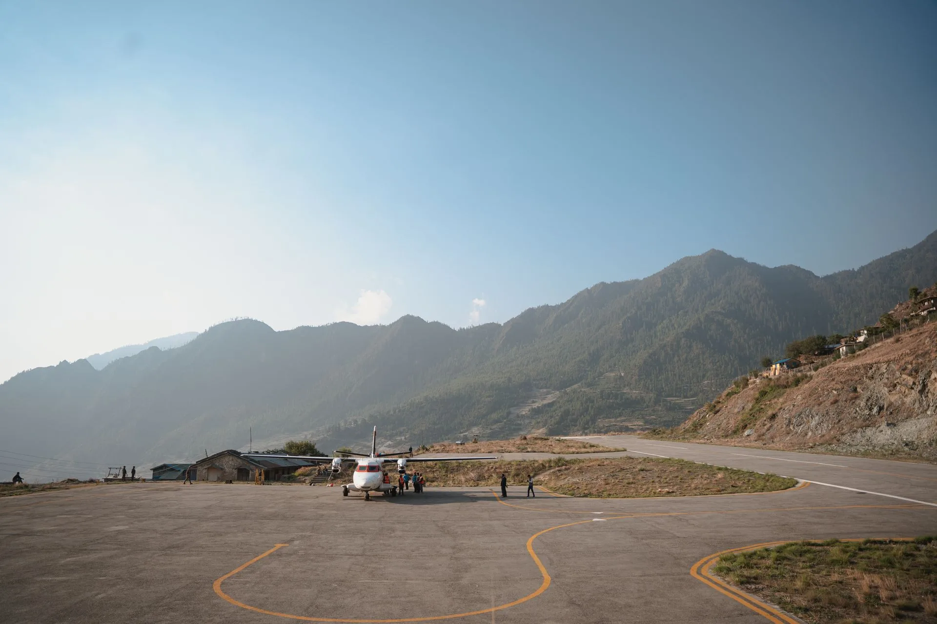 A scenic view of a small aircraft on a lukla airport surrounded by lush green hills under a vibrant blue sky.
