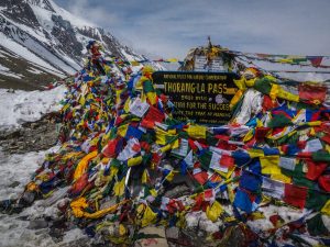 Thorong La Pass (5,416m) in the Annapurna Circuit, Nepal, decorated with vibrant prayer flags against a backdrop of snowy Himalayan peaks.