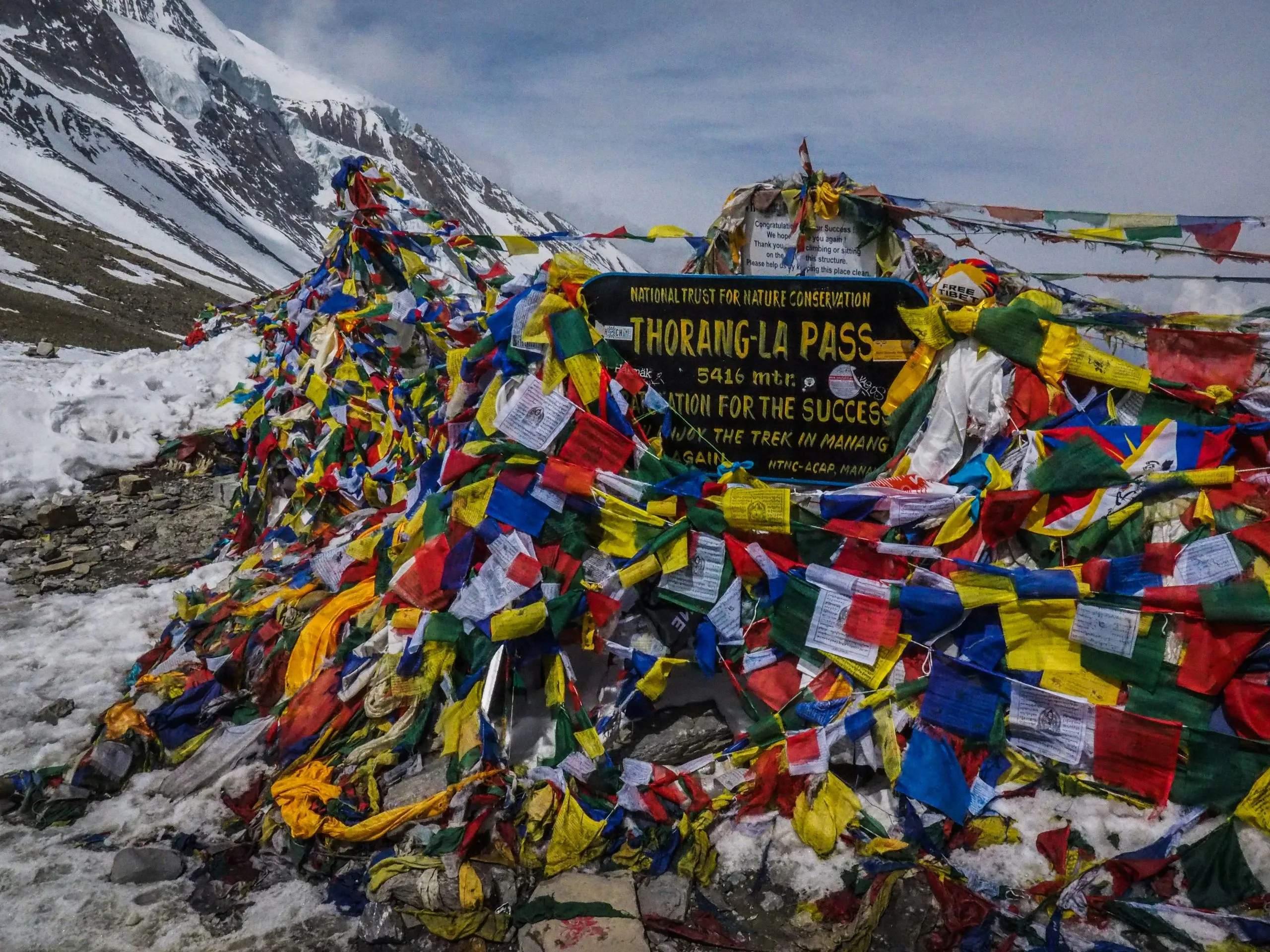 Annapurna Circuit via Thorong La Pass (5,416m) in the Annapurna Circuit, Nepal, decorated with vibrant prayer flags against a backdrop of snowy Himalayan peaks.