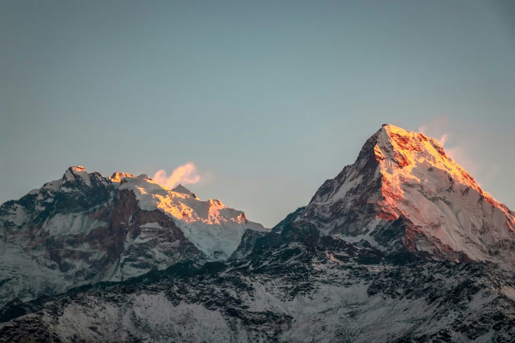 Annapurna mountain range at sunrise, Nepal, with snow-capped Himalayan peaks bathed in golden morning light under a clear blue sky.