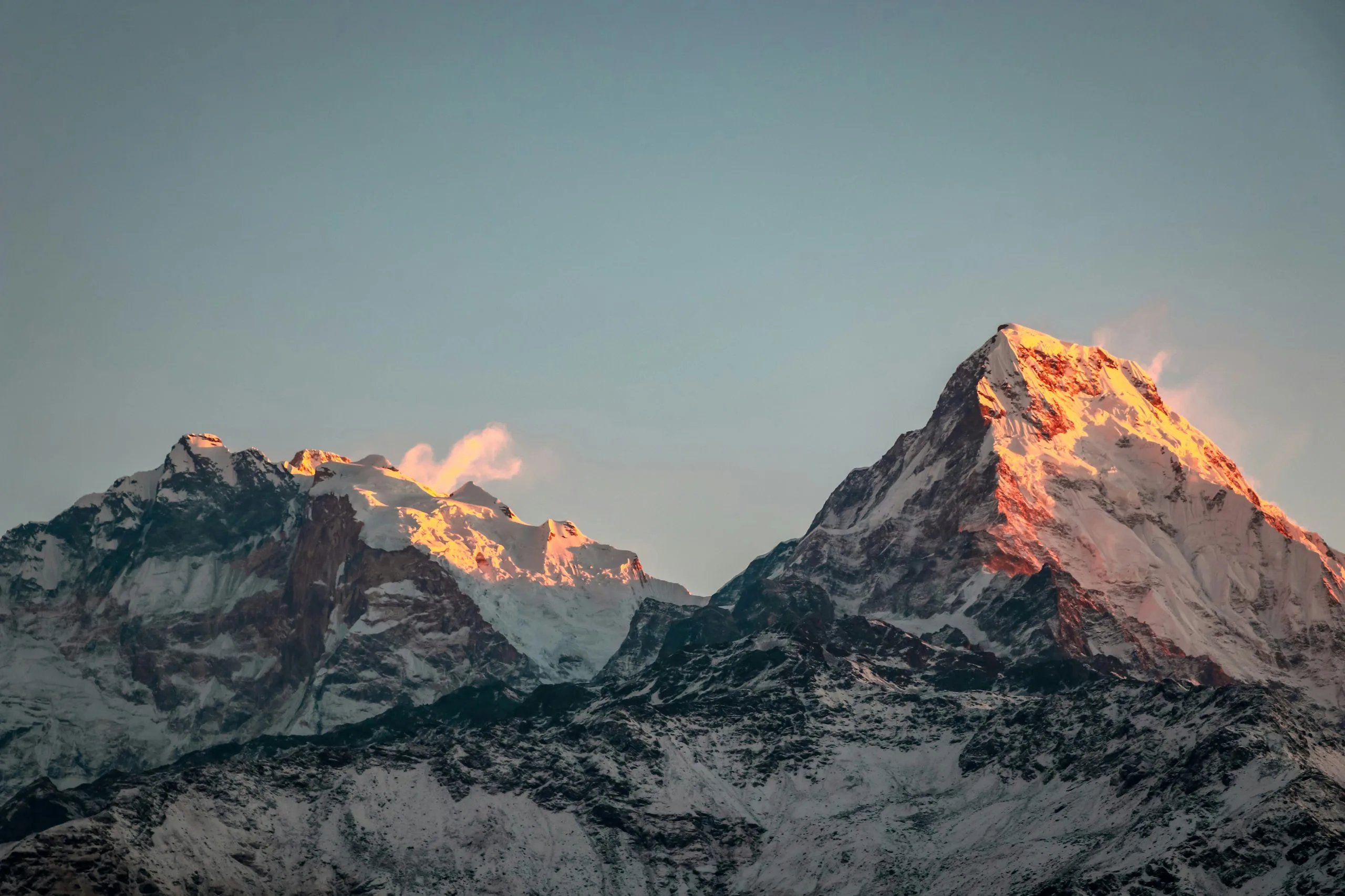Snow-capped peaks of the Annapurna mountain range in Nepal glow with golden sunrise light beneath a clear blue sky, viewed from the Annapurna Circuit Trek.
