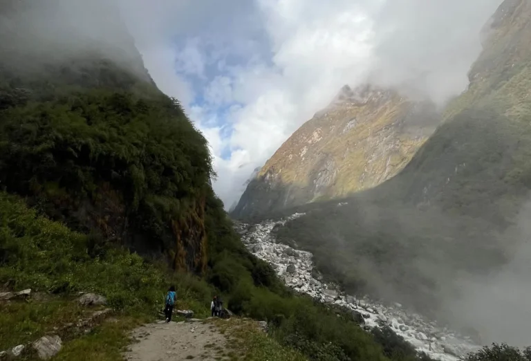 Hikers trekking through a rocky mountain valley in the Himalayas under a cloudy sky.