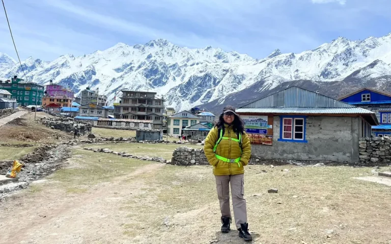 A female trekker in a yellow down jacket and hiking gear stands in Kyangjin Gunj, Langtang Valley, Nepal