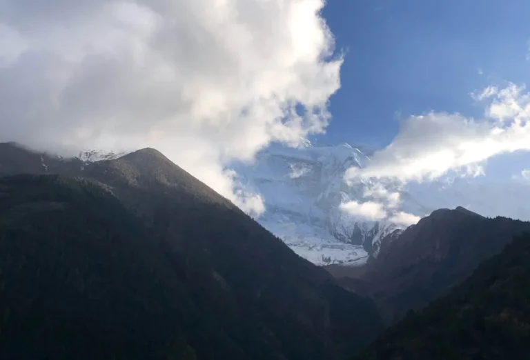 Snow-capped Annapurna mountain peaks partially covered by white clouds under a blue sky in Nepal.