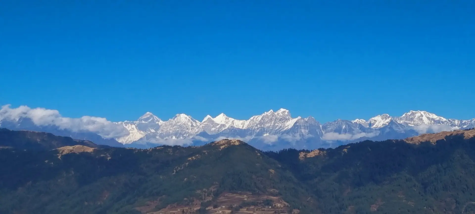 A wide panoramic shot of the snow-capped Himalayan mountain range stretching across a clear blue sky Pikey Peak