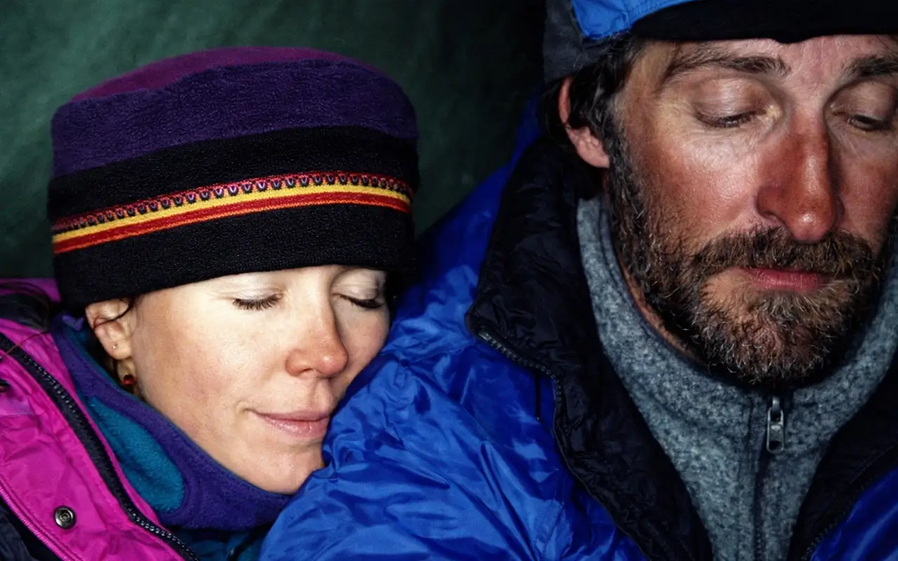 Close-up photo of American mountaineer Francys Arsentiev and her husband Sergei Arsentiev wearing cold-weather gear and beanies, appearing exhausted with closed eyes after a climb.